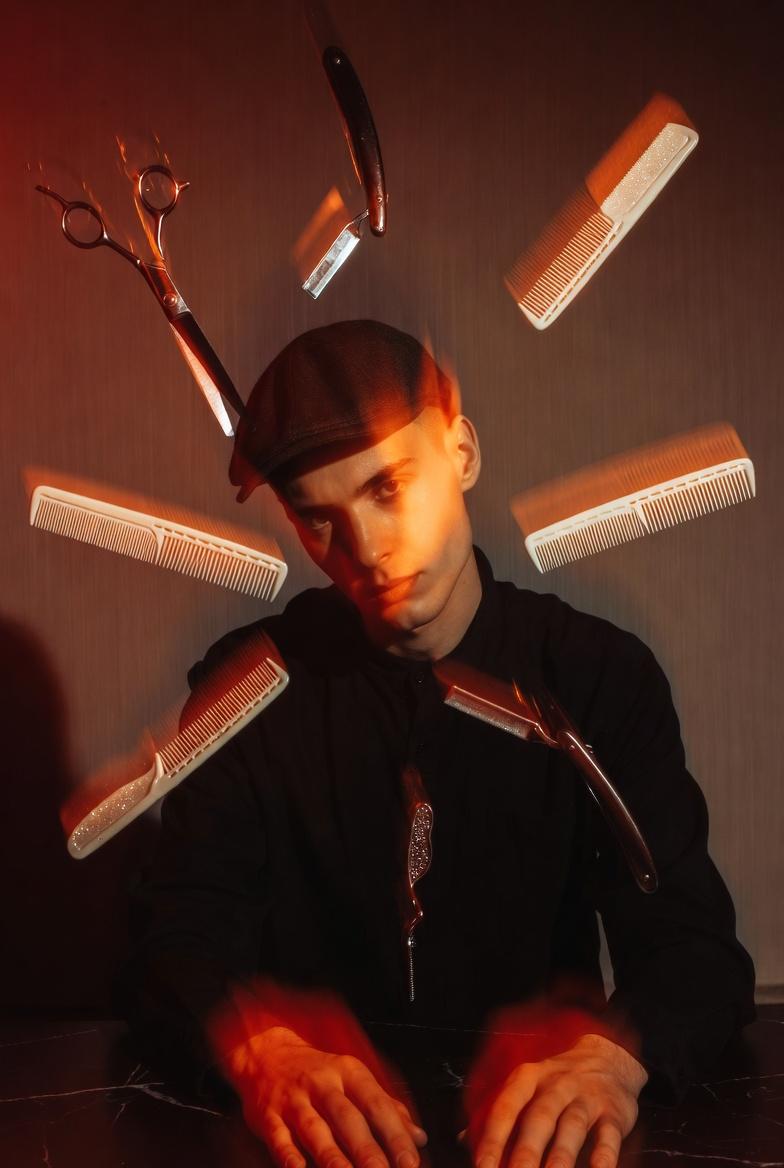 Cinematic portrait of a barber in a flat cap surrounded by floating scissors, razors and combs in red light