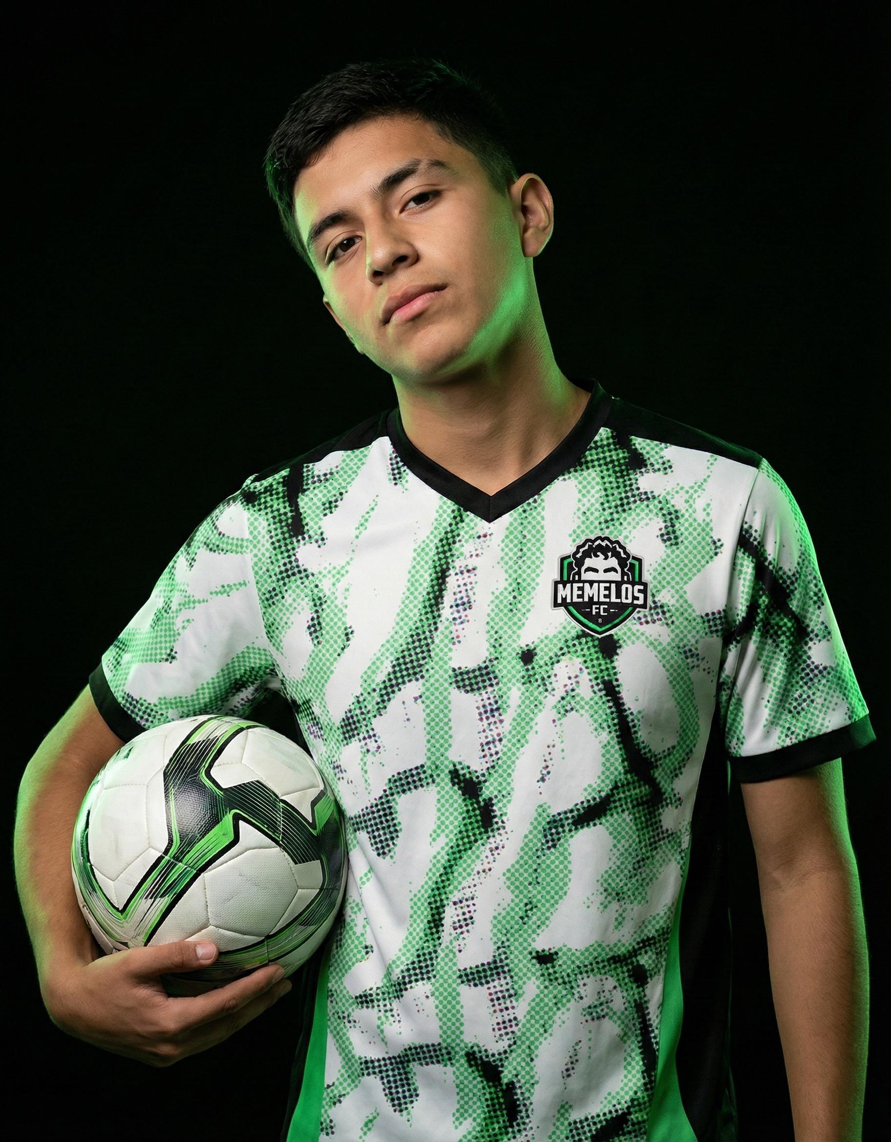 Memelos FC player in the home kit holding a ball under green light