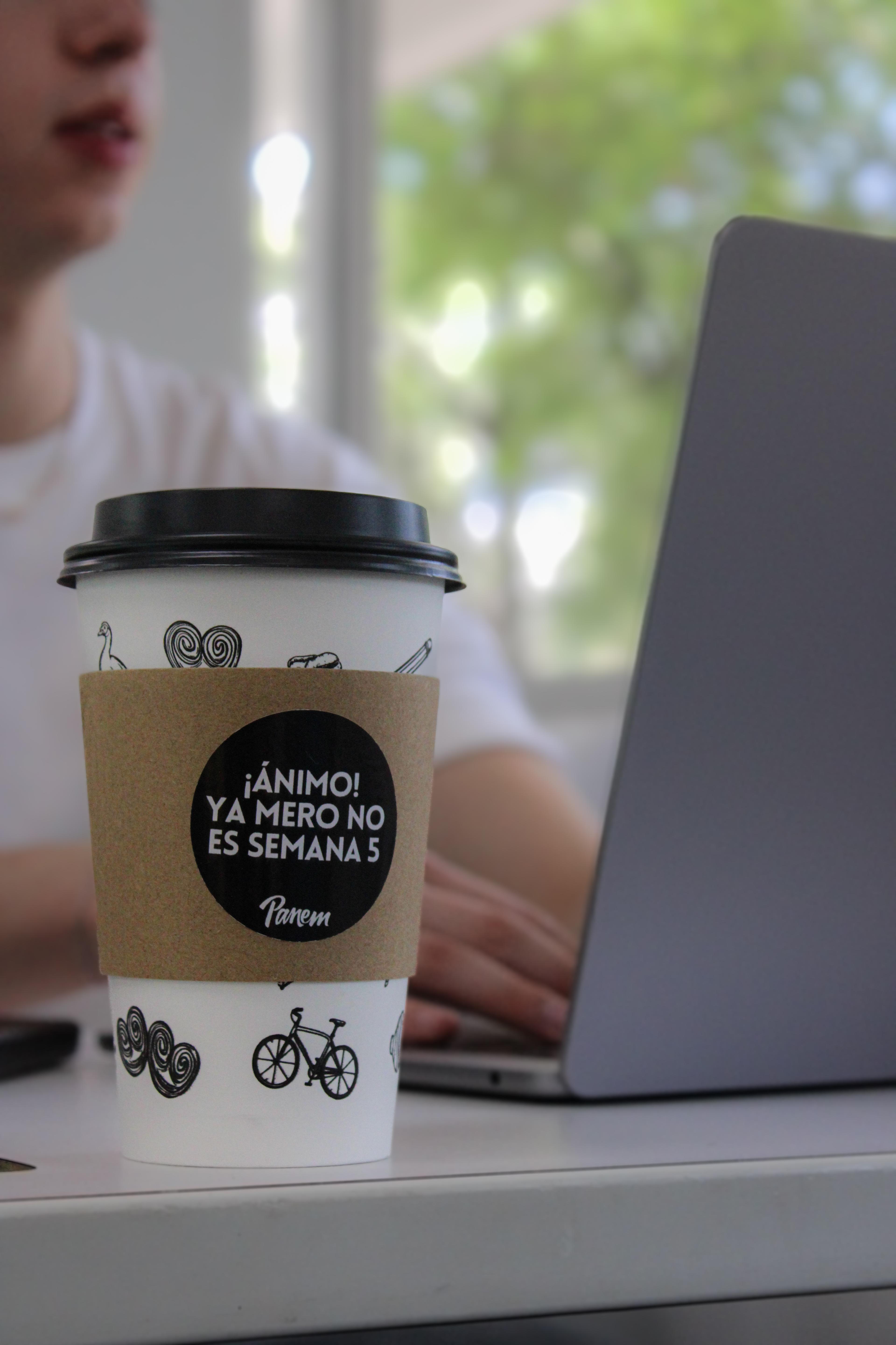 Panem cup with a 'semana 5' sleeve message beside a laptop